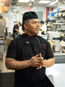 Chef in black uniform in a busy kitchen of an upscale Indian restaurant, Junoon, focused and ready to prepare dishes.