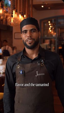 Staff member wearing Junoon apron inside upscale Indian restaurant with warm lighting and elegant decor.