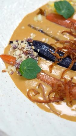 Carrots in a rich creamy sauce with chopped nuts, fried onions, and green garnish on a speckled white plate.