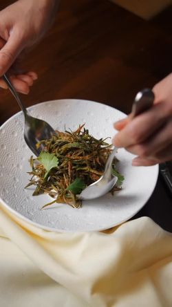 Fried Indian vegetable dish garnished with cilantro leaves served on a textured white plate in an upscale Indian restaurant.
