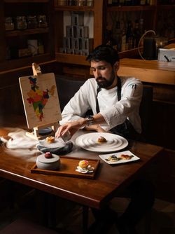 Chef preparing fine dining Indian cuisine dishes with intricate presentation on a wooden table in a dimly lit upscale setting
