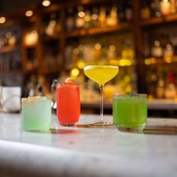 Colorful cocktails displayed on a marble bar counter with blurred bottles and warm lighting in the background at Junoon.
