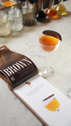 Cocktail with a chocolate garnish beside an open menu displaying a brown-themed drink at Junoon's cocktail bar.