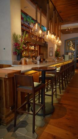 Upscale Indian restaurant bar with wooden stools, pendant lights, and a cocktail bar in a New York fine dining setting.