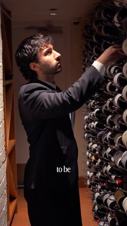 Man in a suit selecting a wine bottle from a large wine rack in an upscale Indian restaurant.