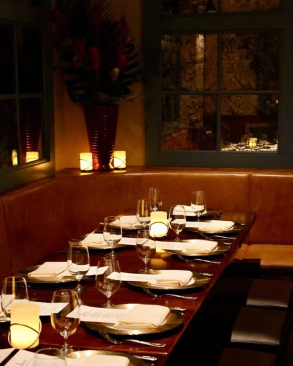 Cozy fine dining area with leather seating, set tables with white napkins, glassware, and ambient candle lighting.
