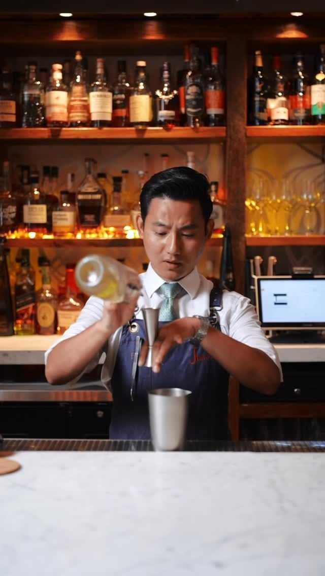 Bartender preparing a cocktail at the bar in an upscale Indian restaurant with a selection of liquor bottles on the shelves.